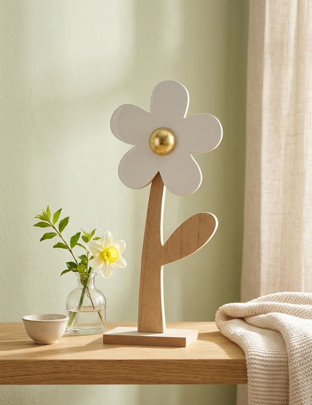 Holzblume Ninni mit Narzisse in Glasvase und Strickdecke vor salbeigrüner Wand