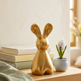 Daggy-Hase in Gold auf hellem Holztisch mit Pastellbüchern, Hyazinthe und Leinentuch