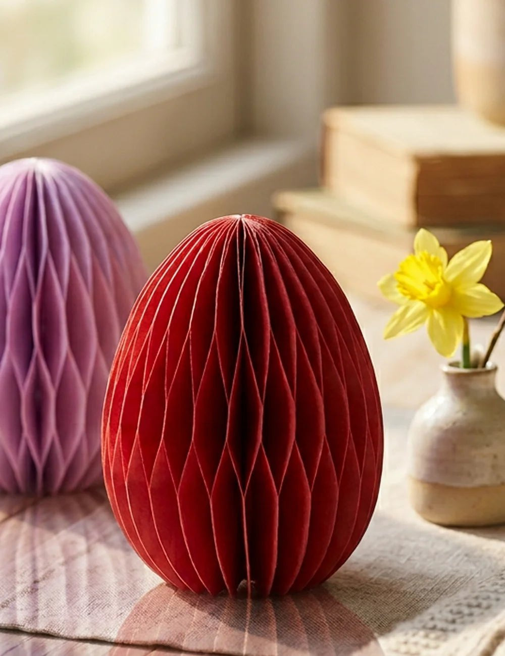 Rotes Waben-Papier-Osterei Eggo auf Leinentuch neben Narzisse in Keramikvase am Fenster