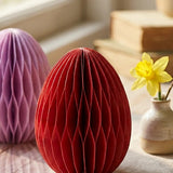 Rotes Waben-Papier-Osterei Eggo auf Leinentuch neben Narzisse in Keramikvase am Fenster