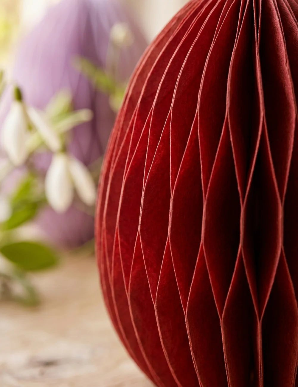 Nahaufnahme rotes Waben-Papier-Ei Eggo mit sichtbarer Falttextur und Lila-Ei im Hintergrund