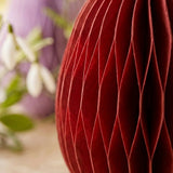 Nahaufnahme rotes Waben-Papier-Ei Eggo mit sichtbarer Falttextur und Lila-Ei im Hintergrund