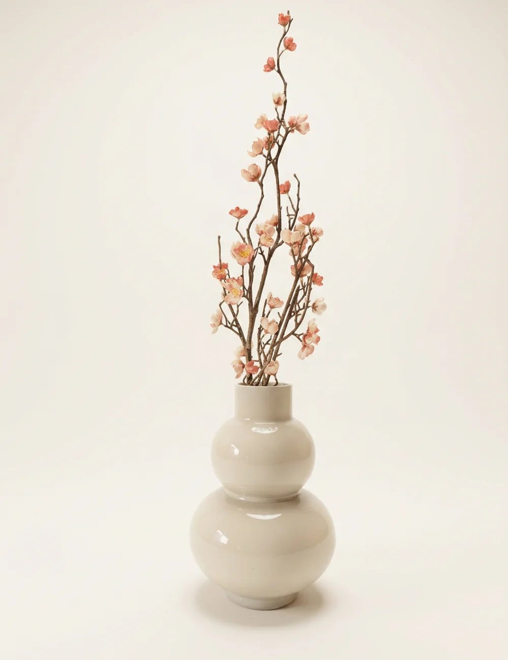 Dekozweig Pfirsichblüte in Vase vor cremefarbenem Hintergrund