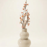 Dekozweig Pfirsichblüte in Vase vor cremefarbenem Hintergrund