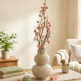 Dekozweig Pfirsichblüte rosa in Keramikvase auf Holztisch mit Büchern und Teelicht