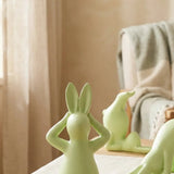 Meditierender Yoga-Hase frontal mit sitzender und sich verbeugender Figur im Hintergrund